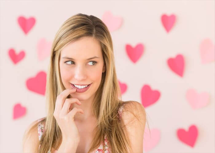 Shy beautiful woman looking away with heart shaped papers stuck against pink background