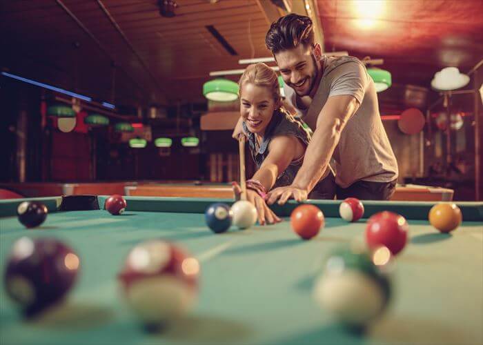 Happy couple having fun while playing snooker in a pool hall.