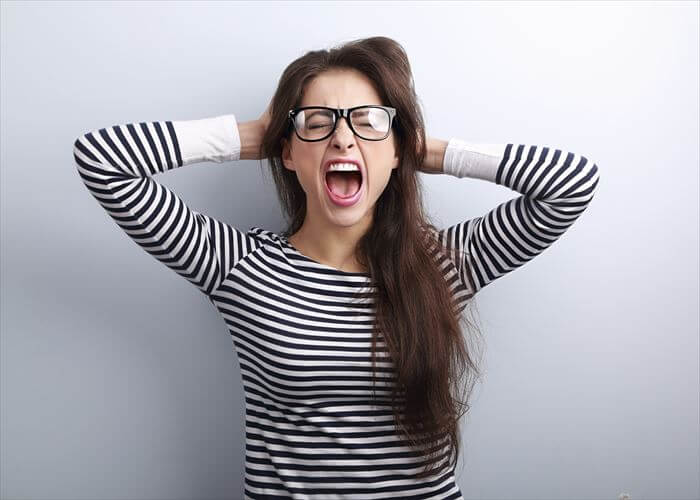 Anger young business woman in glasses strong screaming with wild open mouth and holding head the hands on blue background