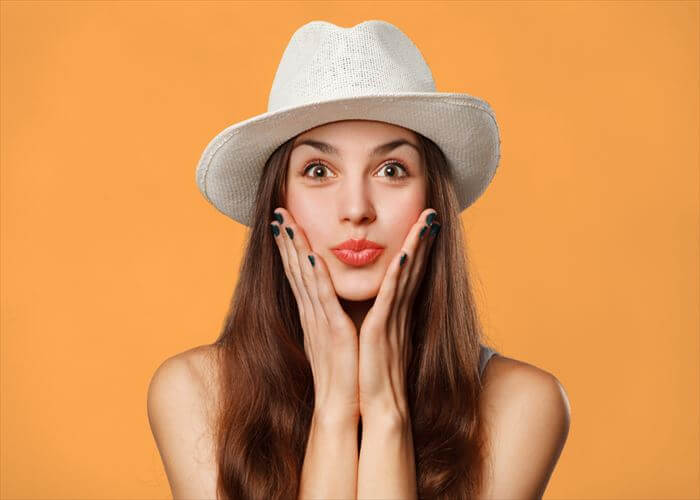 Surprised happy beautiful woman looking sideways in excitement. Excited girl in hat, isolated on orange background