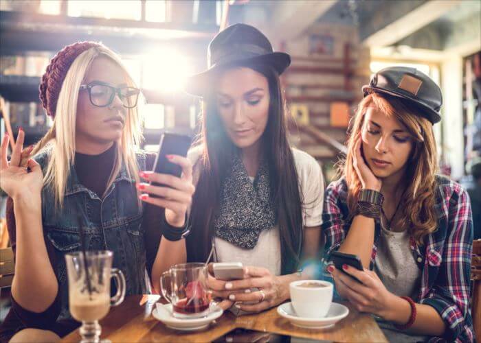 Female friends sitting in a cafe while each of them is using their own cell phone.